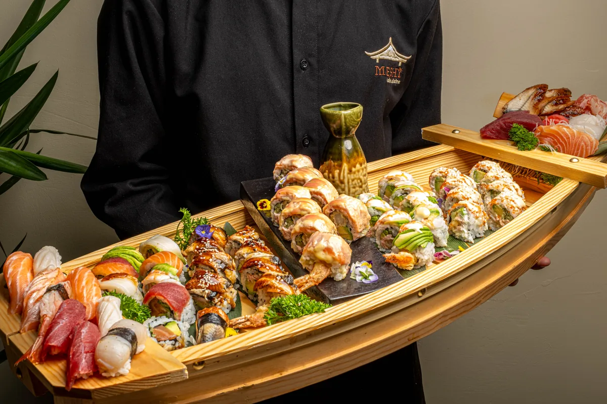 Obsluha nese dřevěnou loď plnou sushi — maki, nigiri i sashimi